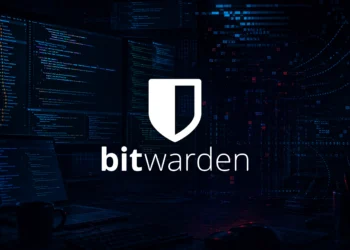 Dark cyberpunk-style developer workspace with multiple monitors displaying code in a dimly lit environment, featuring Bitwarden logo
